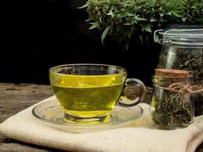 Cannabis tea in a clear glass cup with a marijuana bud in a jar on a wooden and the black background